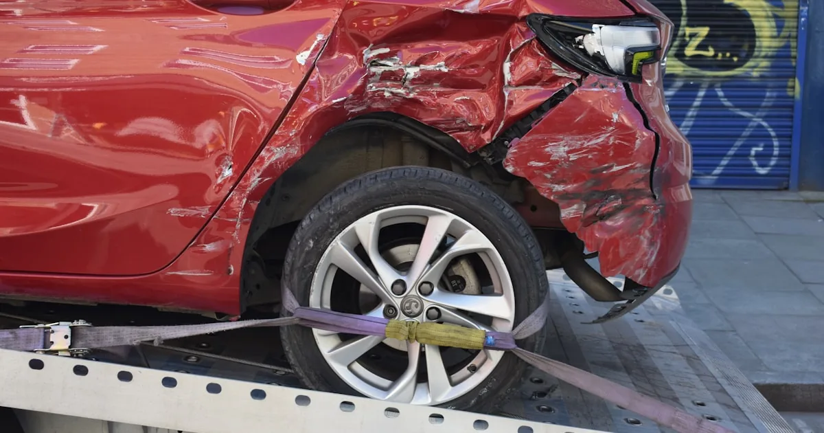 Mașină roșie avariată lateral, urcată pe platforma unui tractor auto